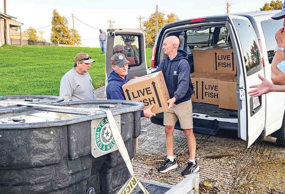 Texas Parks & Wildlife Department’s (TPW) Inland Fisheries Jasper District Supervisor Todd Driscoll hands a box containing 50,000 fry to TPW Inland Fisheries Biologist Dan Ashe as TPW Technician Ray Lenderman waits in the wings. Two million fry are being released into Lake Livingston through a stocking program that is a joint effort of many, including Texas Parks & Wildlife Department, Trinity River Authority, Lake Livingston Fishing Club aka “The Happy Hookers,” Friends of Lake Livingston and local fishing guides Michael Richardson and Jeff Friederich. Photo by Emily  Banks Wooten