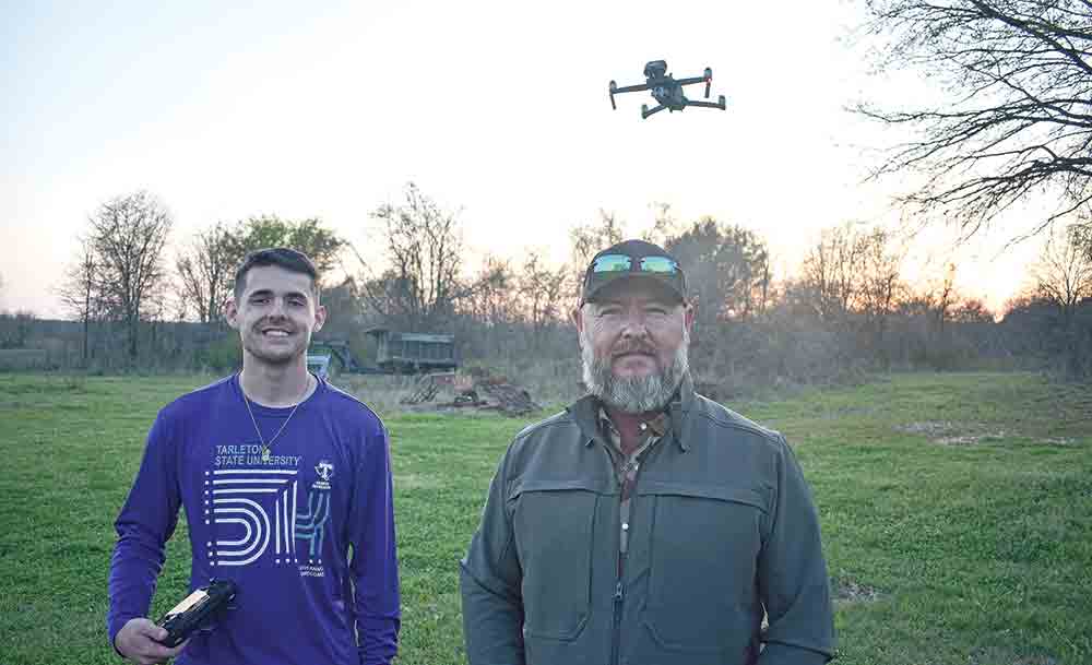 Logan Rice (left) and his dad Lawrance Rice with their drone hovering in the background, about to scout a distant field for wild hogs. Photo by Luke Clayton